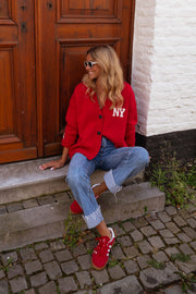Gilet ample boutonné rouge porté par une femme, assise, marches en pierre, baskets rouges