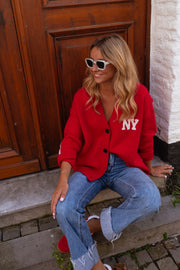 Gilet ample boutonné rouge porté par une femme, assise, marches, lunettes