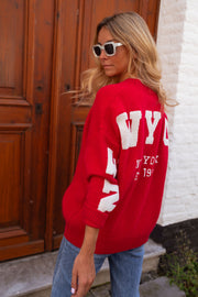Gilet ample boutonné rouge porté par une femme, vue de dos, lettres blanches, porte en bois