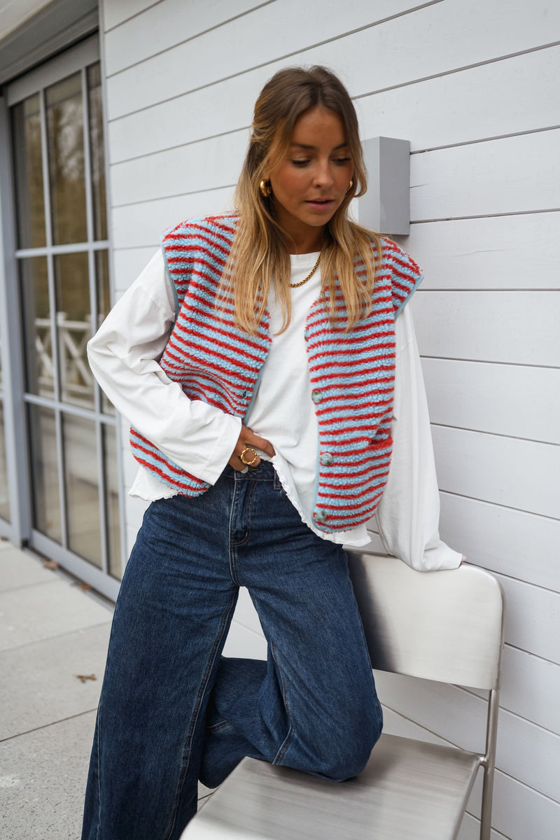 Gilet sans manches à poches porté par une femme, assise, chaise blanche, jean foncé