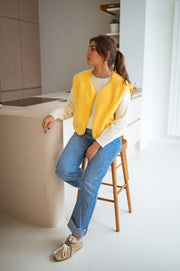 Gilet court à poches jaune porté par une femme, silhouette entière, jean droit, comptoir