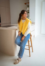 Gilet court à poches jaune porté par une femme, vue de trois-quarts, main dans les cheveux, comptoir