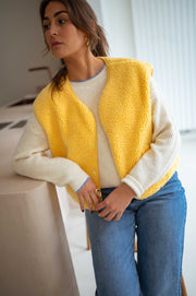 Gilet court à poches jaune porté par une femme, vue rapprochée, cheveux détachés, chemise blanche