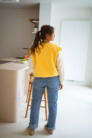 Gilet court à poches jaune porté par une femme, assise, assise sur un tabouret, jean