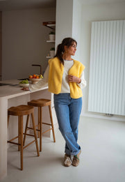 Gilet court à poches jaune porté par une femme, vue de face, comptoir, tabouret en bois