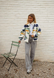 Gilet polaire zippé à motifs écru porté par une femme, vue de face, chaise verte, jean gris