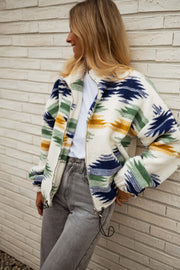 Gilet polaire zippé à motifs écru porté par une femme, vue de face, col montant, mur