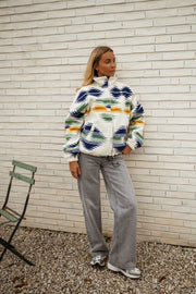 Gilet polaire zippé à motifs écru porté par une femme, vue de face, mains dans les poches, mur blanc