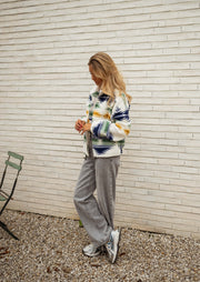 Gilet polaire zippé à motifs écru porté par une femme, silhouette entière, chaise pliante, mur blanc
