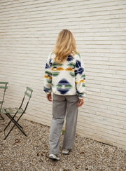 Gilet polaire zippé à motifs écru porté par une femme, vue de dos, mur blanc, cheveux blonds