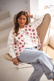 Gilet fleuri effet mouton porté par une femme, assise, fauteuil en rotin, jean clair