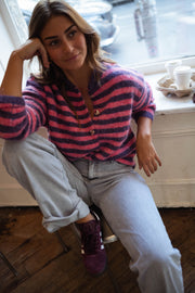 Gilet rayé à boutons cœur porté par une femme, assise, tabouret, baskets violettes