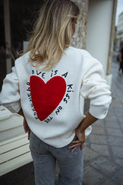 Gilet à manches longues écru porté par une femme, vue rapprochée, grand cœur rouge, banc blanc
