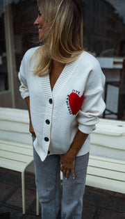 Gilet à manches longues écru porté par une femme, vue de face, banc blanc, cœur rouge