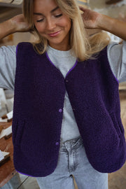 Gilet mouton court sans manches mauve porté par une femme, vue rapprochée, boutons-pression, cheveux blonds