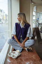 Gilet mouton court sans manches mauve porté par une femme, assise, rebord de fenêtre, baskets blanches