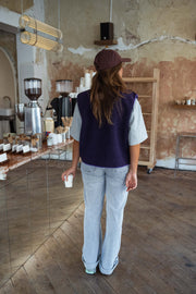 Gilet mouton court sans manches mauve porté par une femme, vue de dos, casquette, café