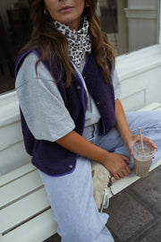 Gilet mouton court sans manches mauve porté par une femme, assise, banc blanc, foulard