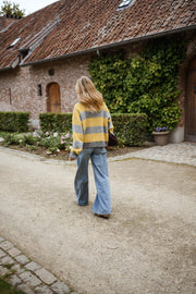 Gilet rayé zippé col montant porté par une femme, silhouette entière, allée de gravier, jean bleu