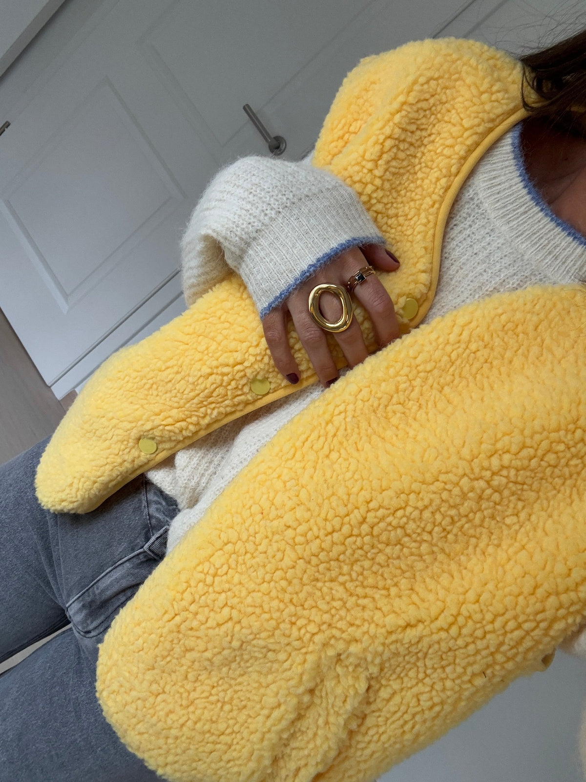 Gilet court à poches jaune porté par une femme, vue rapprochée, manche en laine bouclée, détail