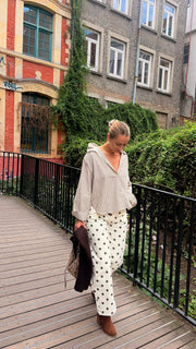 Pantalon à pois porté par une femme, silhouette entière, rambarde, blouse crème