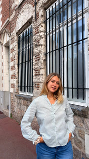 Chemise rayée à manches bouffantes portée par une femme, silhouette entière, mur de briques, fenêtre