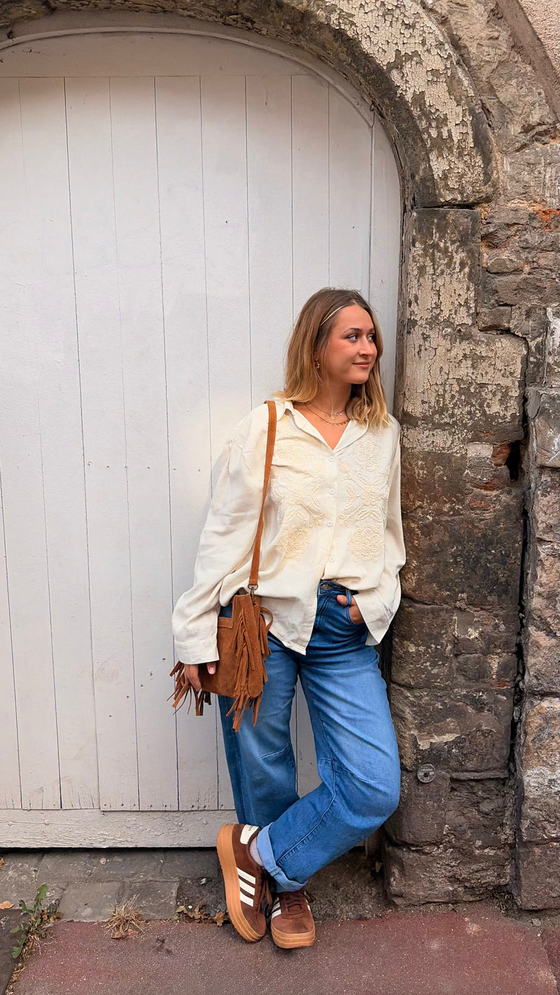 Chemise en lin brodée portée par une femme, silhouette entière, porte blanche, sac