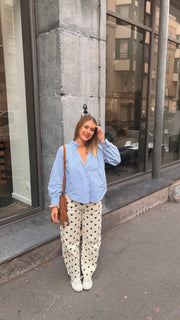 Chemise à col volanté portée par une femme, vue de trois-quarts, chemise bleu clair, pantalon à pois