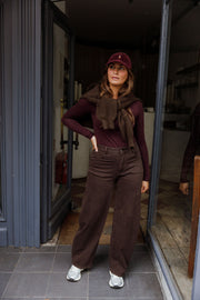 Jean ample coupe ballon porté par une femme, silhouette entière, pull bordeaux, casquette, devant une vitrine