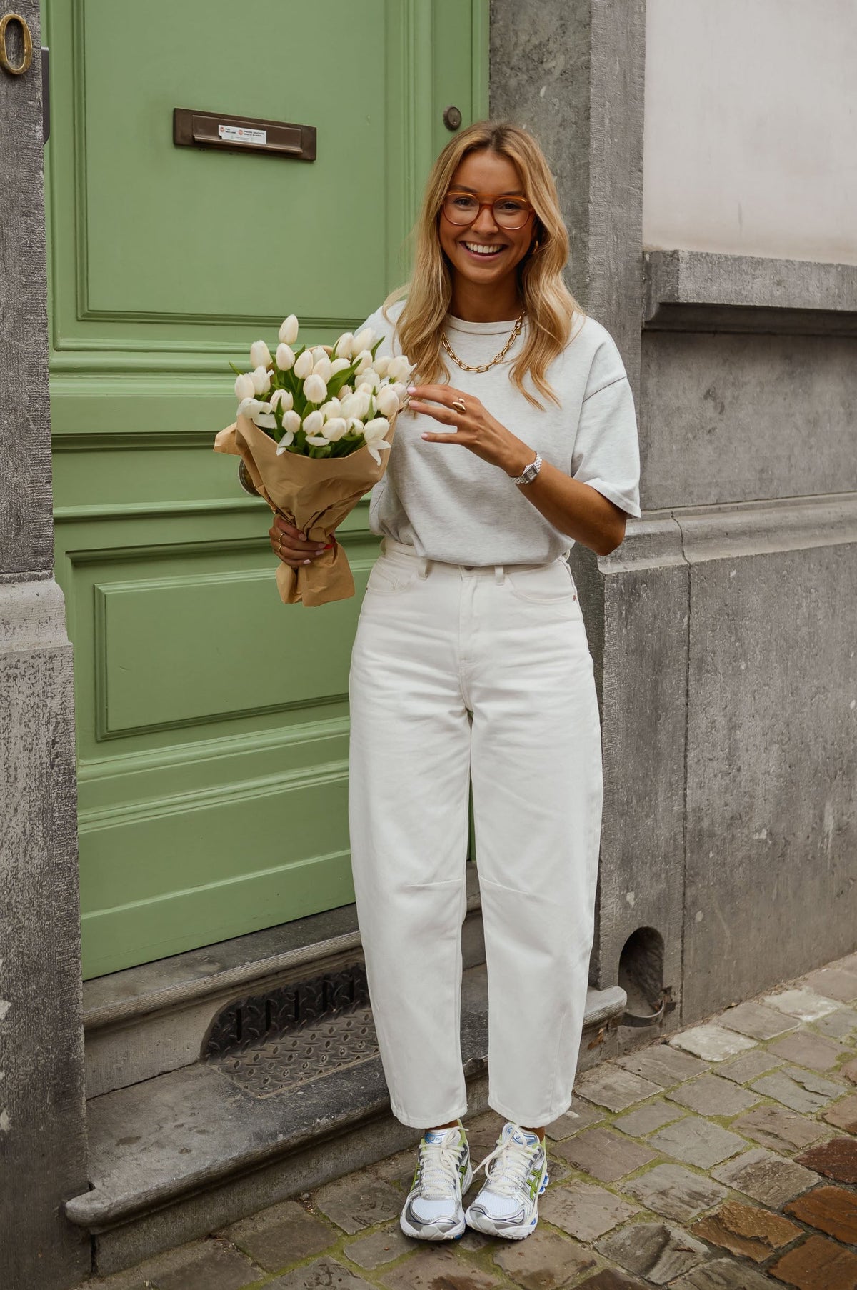 Jean coupe mom légèrement loose porté par une femme, silhouette entière, porte verte, bouquet de fleurs