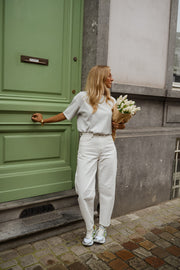 Jean coupe mom légèrement loose porté par une femme, vue de trois-quarts, porte verte, bouquet