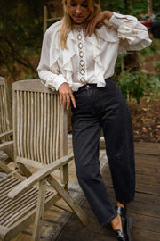 Jeans mom coupe loose porté par une femme, silhouette entière, chemise blanche, chaise en bois