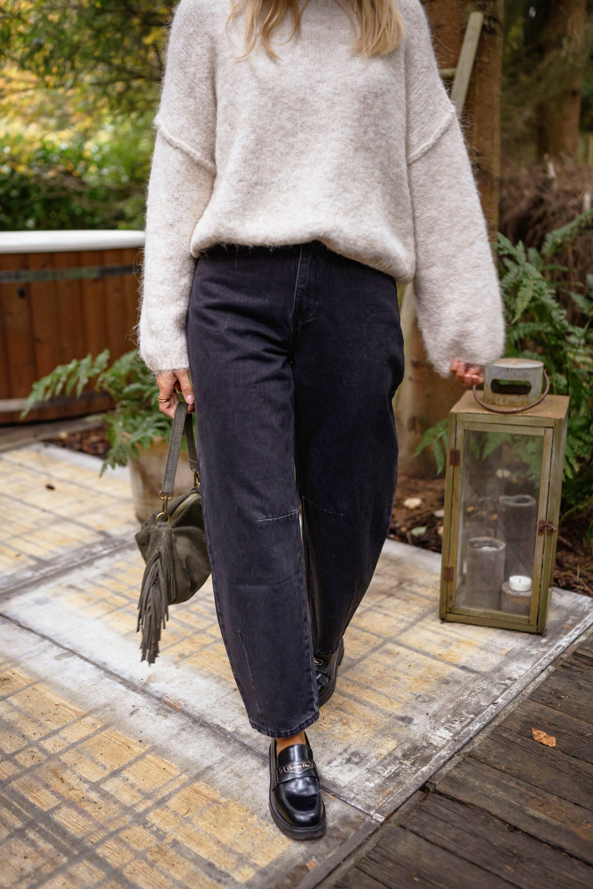 Jeans mom coupe loose porté par une femme, silhouette entière, pull ivoire, terrasse en bois