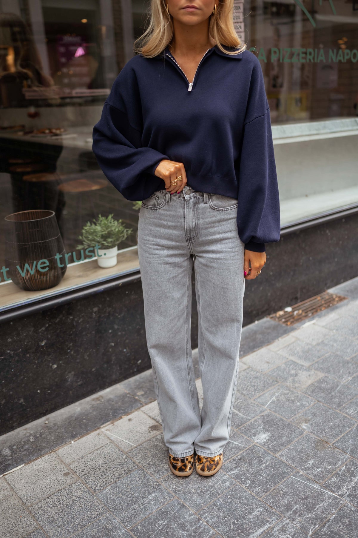 Jean flare taille haute porté par une femme, silhouette entière, pull bleu marine, vitrine