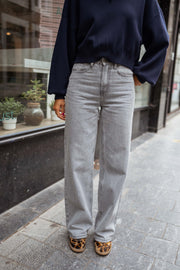 Jean flare taille haute porté par une femme, vue rapprochée, pull marine, jean gris clair
