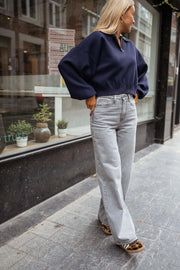 Jean flare taille haute porté par une femme, vue de trois-quarts, pull bleu marine, trottoir