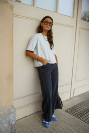 Jeans large effet ballon porté par une femme, silhouette entière, t-shirt blanc, adossée