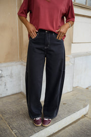 Jeans large effet ballon porté par une femme, vue rapprochée, haut bordeaux, mains dans les poches