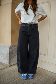 Jeans large effet ballon porté par une femme, silhouette entière, t-shirt blanc, mains sur les hanches
