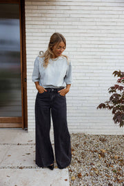 Jean large à coupe loose porté par une femme, silhouette entière, haut bleu clair, porte, de face