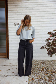 Jean large à coupe loose porté par une femme, silhouette entière, haut bleu clair, main dans les cheveux