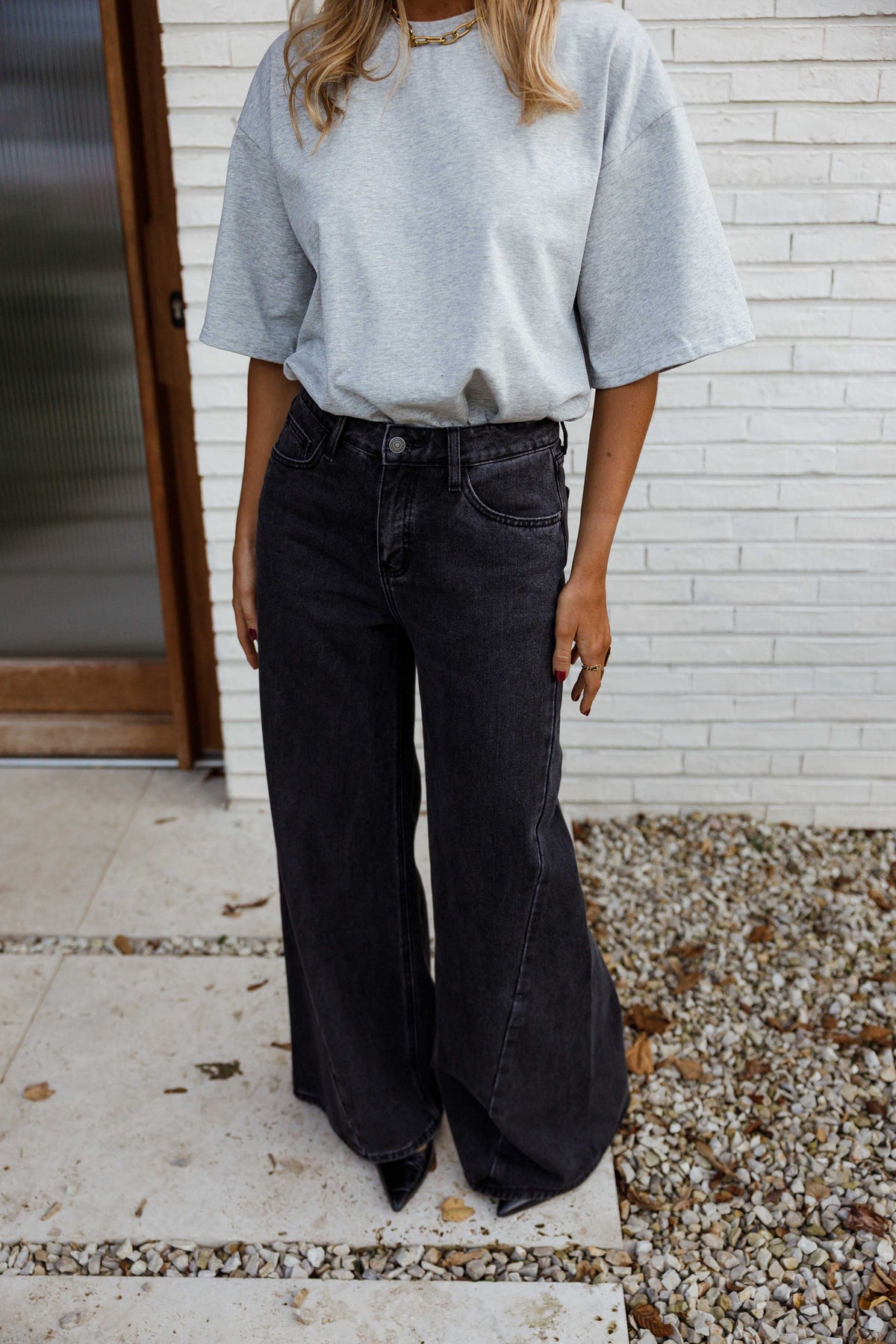 Jean large à coupe loose porté par une femme, silhouette entière, haut bleu clair, mur blanc