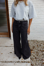 Jean large à coupe loose porté par une femme, silhouette entière, haut bleu clair, mur blanc