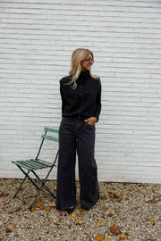 Jean large à coupe loose porté par une femme, vue de profil, haut noir, chaise