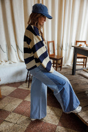 Jean large à côtés bicolores porté par une femme, vue de profil, pull rayé, casquette