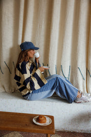 Jean large à côtés bicolores porté par une femme, assise, au sol, casquette