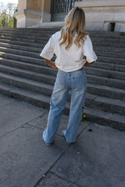 Jeans à étoiles perlées évasé porté par une femme, vue de dos, t-shirt blanc, escalier