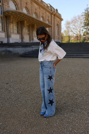Jeans à étoiles perlées évasé porté par une femme, silhouette entière, de loin, étoiles