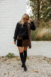 Jupe en daim à damier portée par une femme, silhouette entière, bottes noires, mur blanc