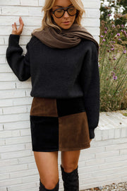 Jupe en daim à damier portée par une femme, vue de trois-quarts, pull noir, écharpe marron, mur blanc